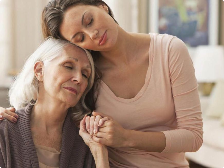 A younger woman gently embraces and holds hands with an older woman, both with peaceful expressions, symbolizing trust, compassion, and support in dementia caregiving.