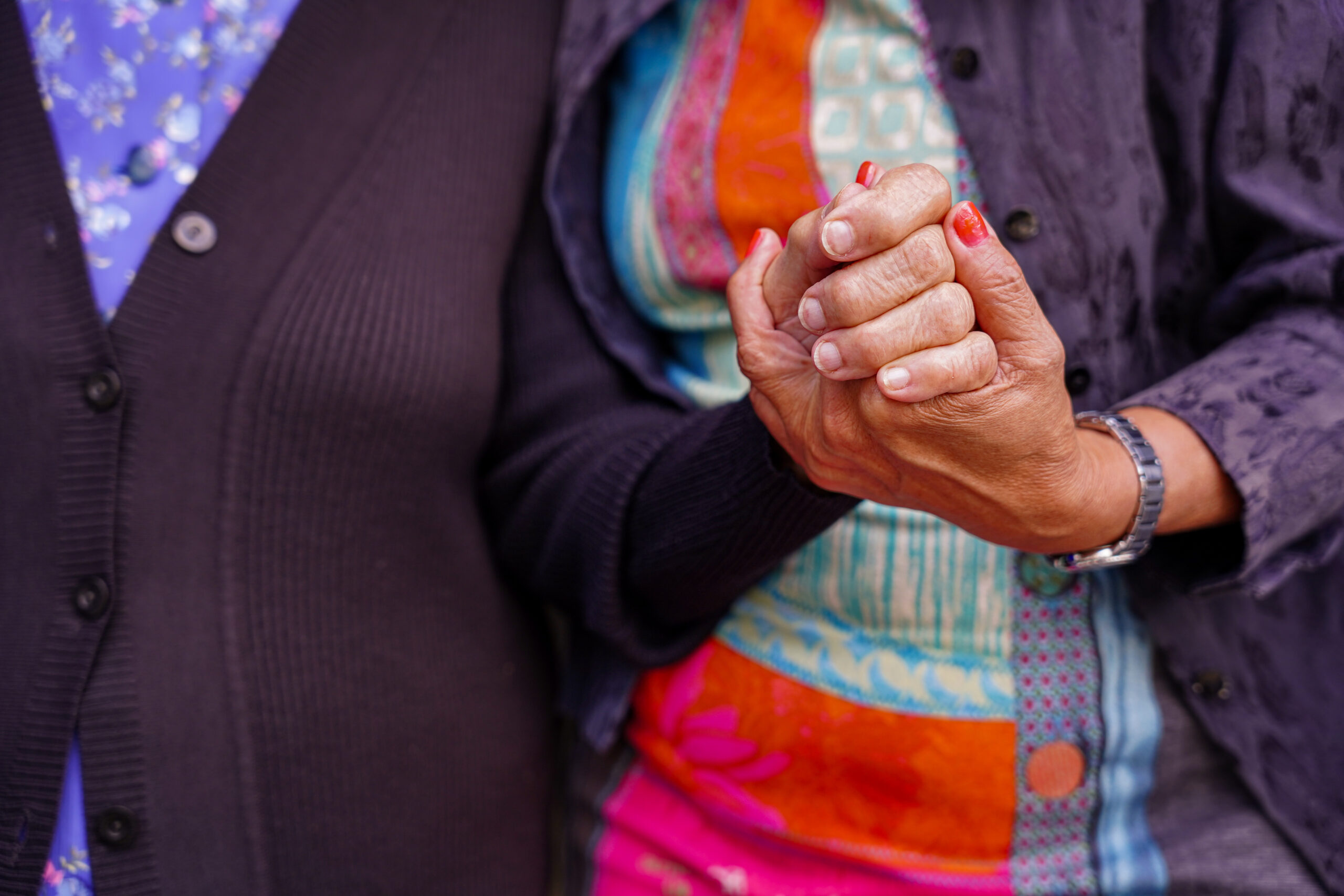 Close-up of two people holding hands, one wearing a colorful shirt and watch, symbolizing trust, support, and compassionate connection in dementia care.