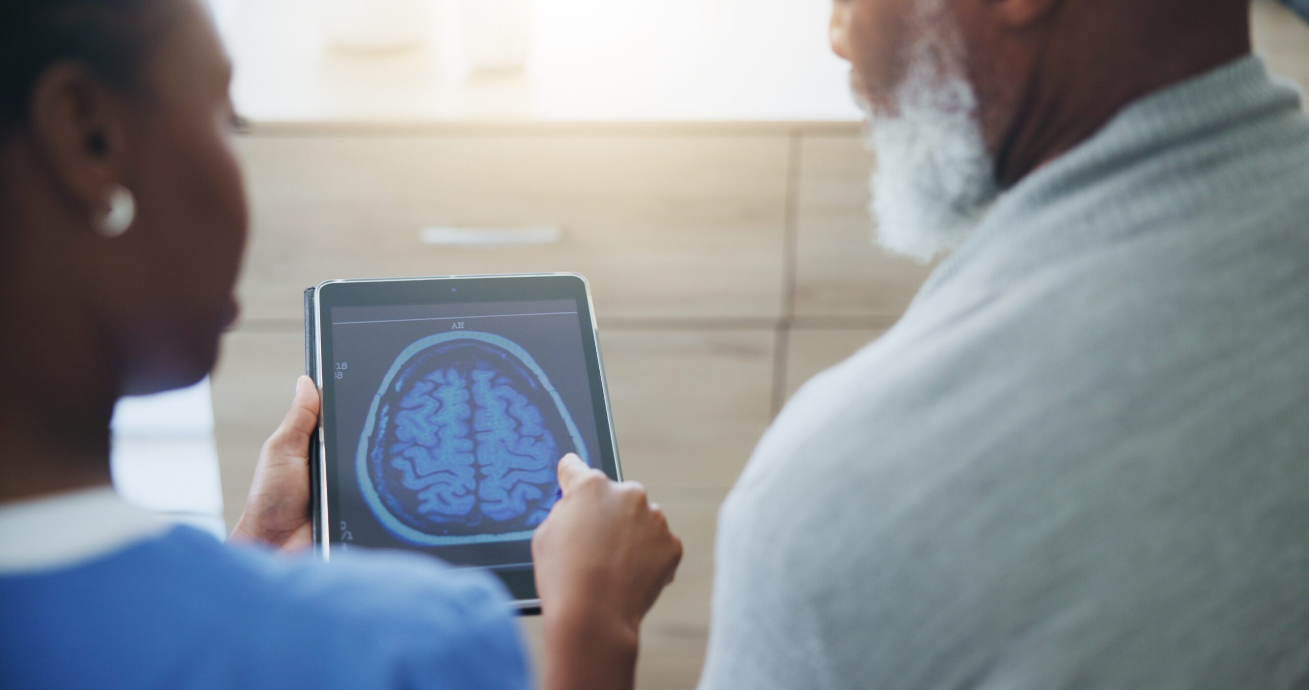 Healthcare professional showing a brain scan on a tablet to an older adult patient, representing brain health education and support for Alzheimer’s care at CaringKind.