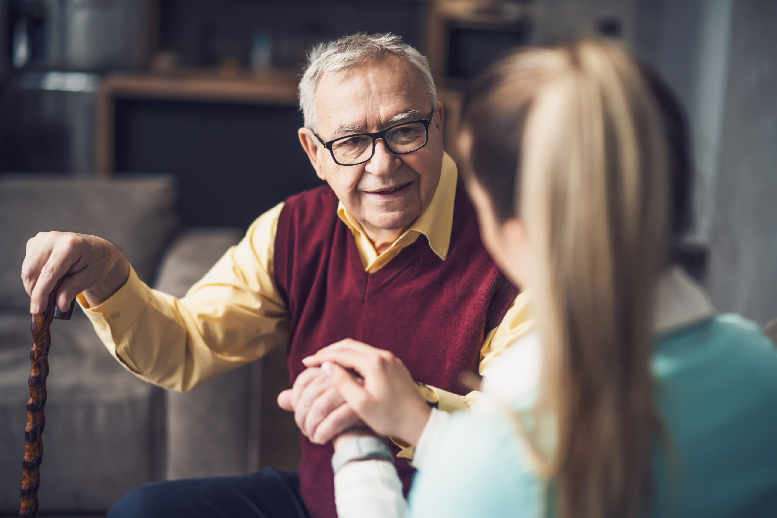 Elderly man holding hands with a dementia specialist in his home.