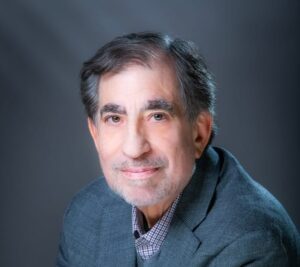 Man posing for a headshot in a suit and with a dark background.