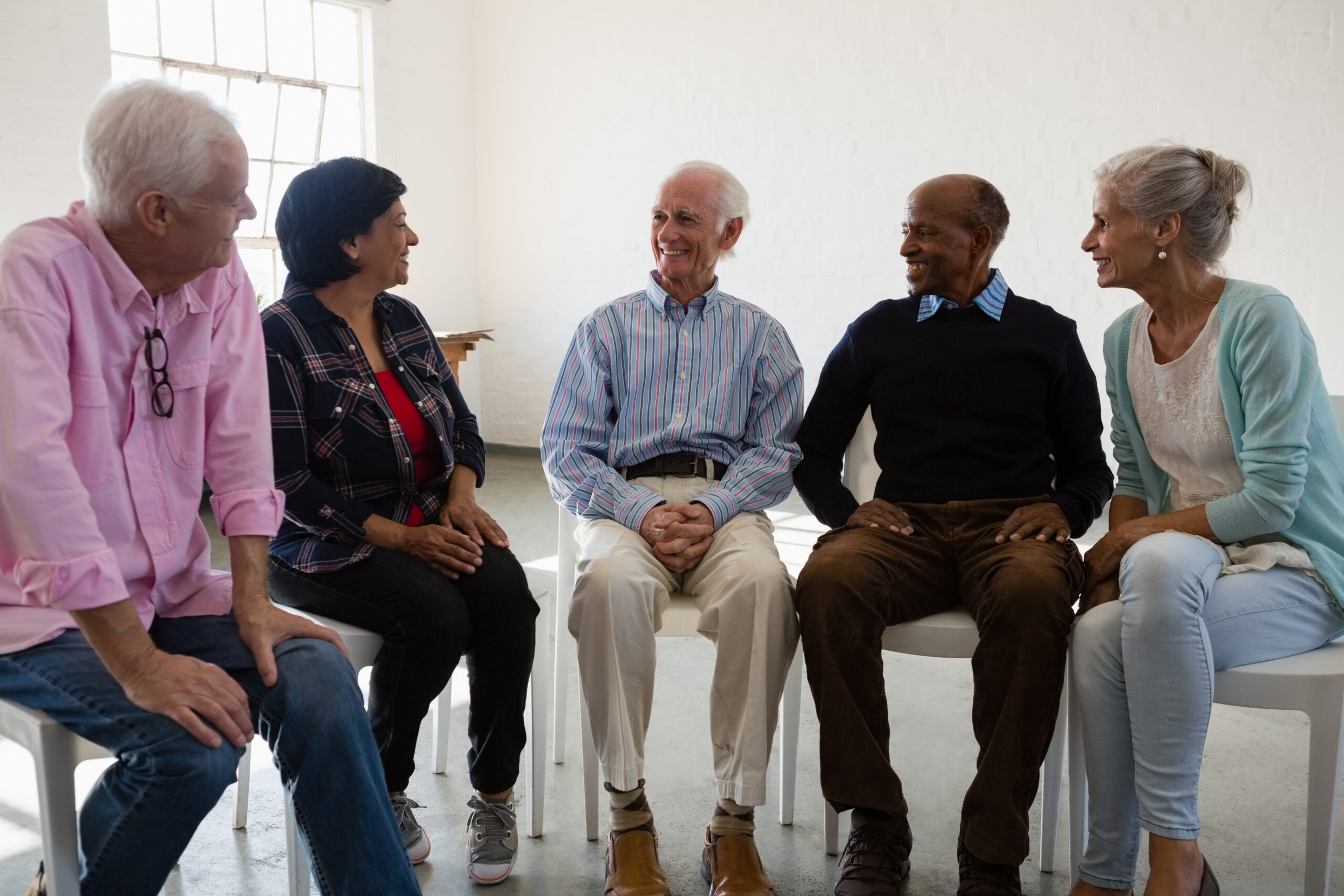 Five older adults sit in a circle having a group discussion during a dementia and Alzheimer’s support meeting at CaringKind.